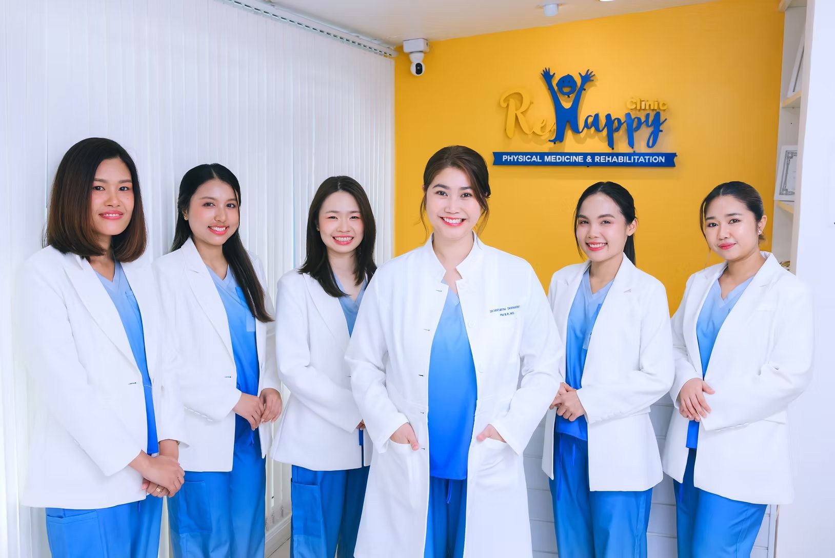 ทีมแพทย์และนักกายภาพบำบัดของ ReHappy Clinic ยืนหน้าโลโก้คลินิก