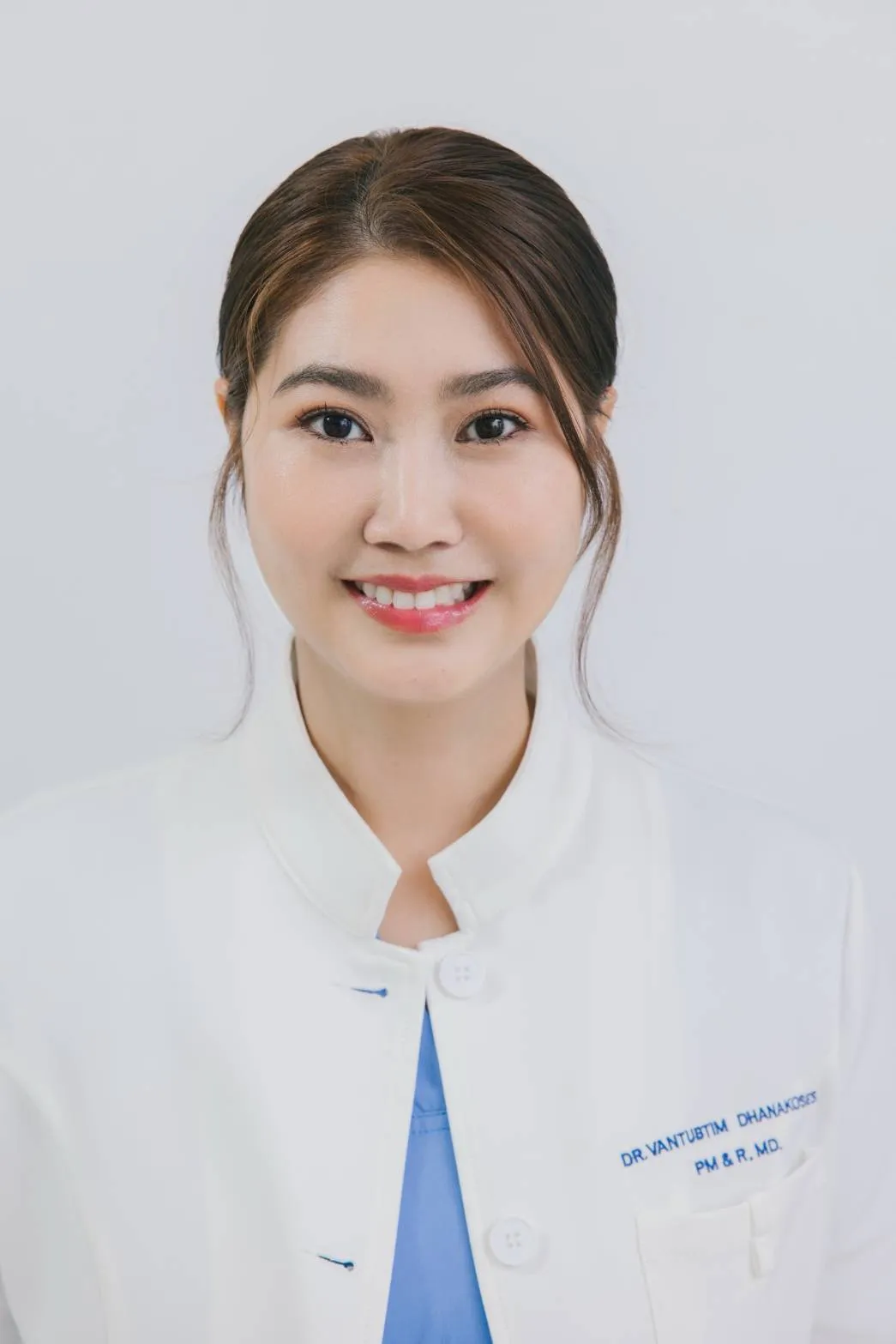แพทย์หญิงแหวนทับทิม ธนโกเศศ เจ้าของ ReHappy Clinic ในเสื้อกาวน์ปักชื่อ ยิ้มหน้าฉากสีขาว